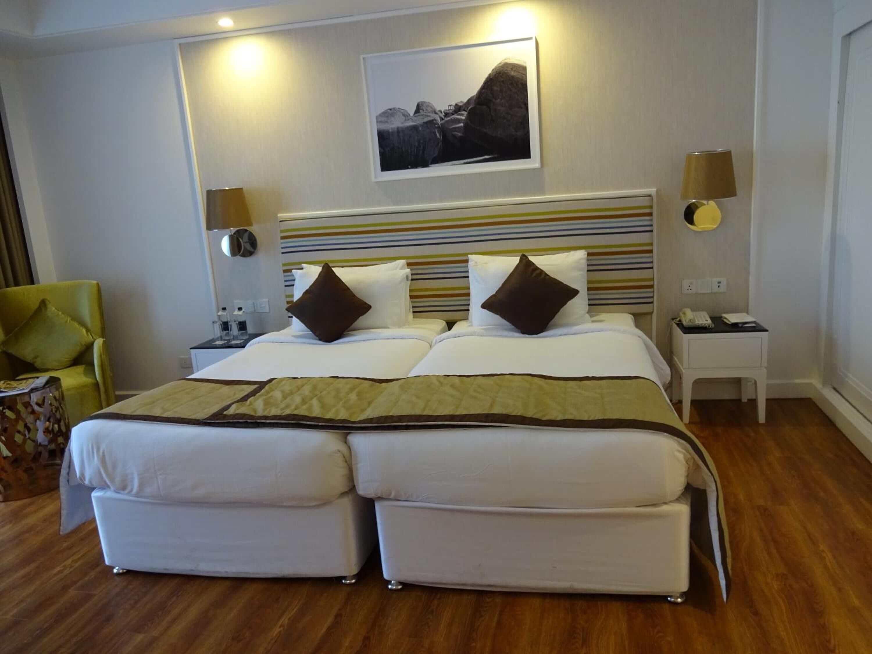 Une chambre d’hôtel avec un grand lit, deux tables de chevet, une chaise et un tableau encadré au mur.