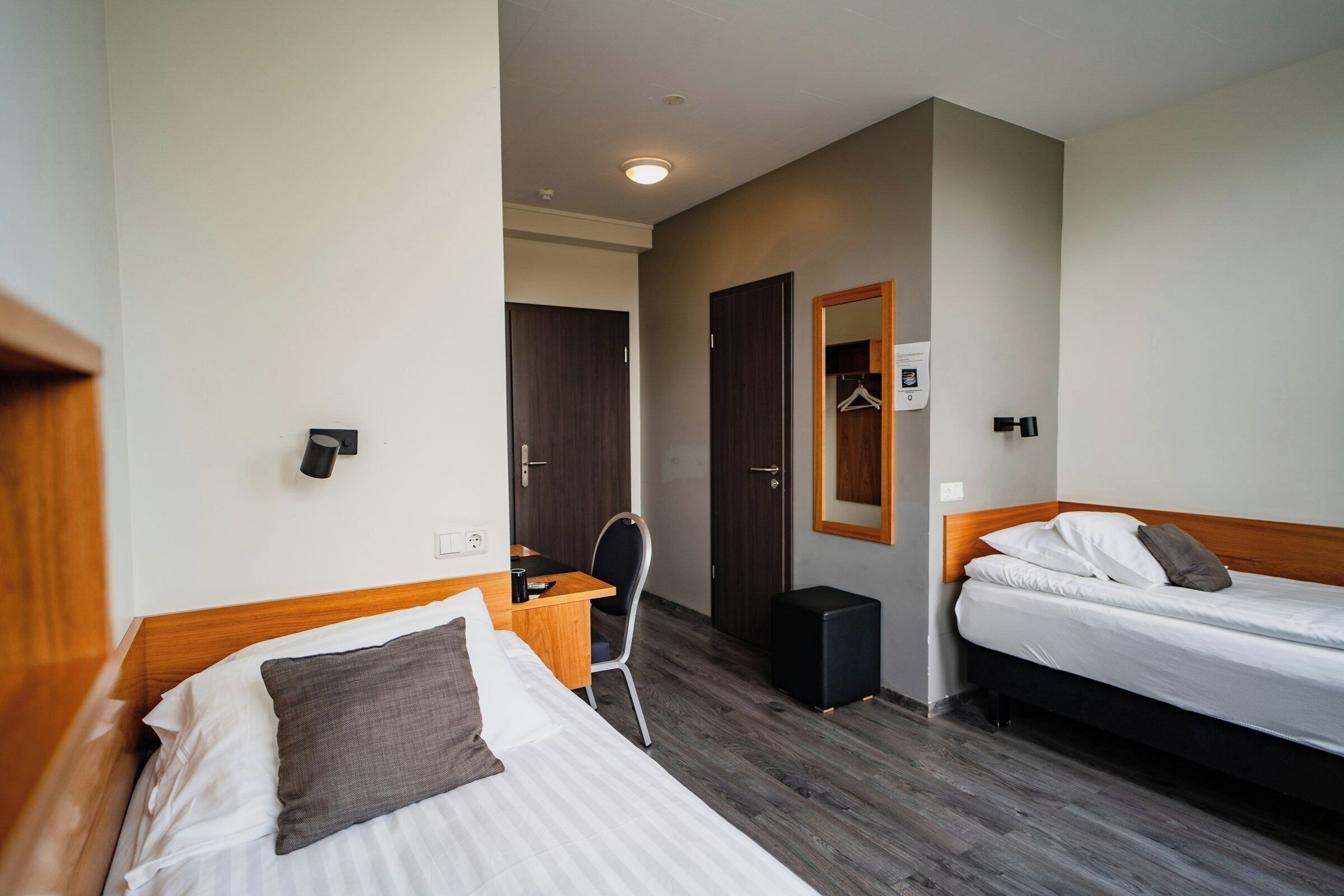Habitación de hotel con dos camas, un escritorio, una silla, un armario y un espejo.