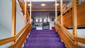 Una escalera con barandas de madera y alfombra morada que lleva a un área de recepción con mostrador y vistas del interior.