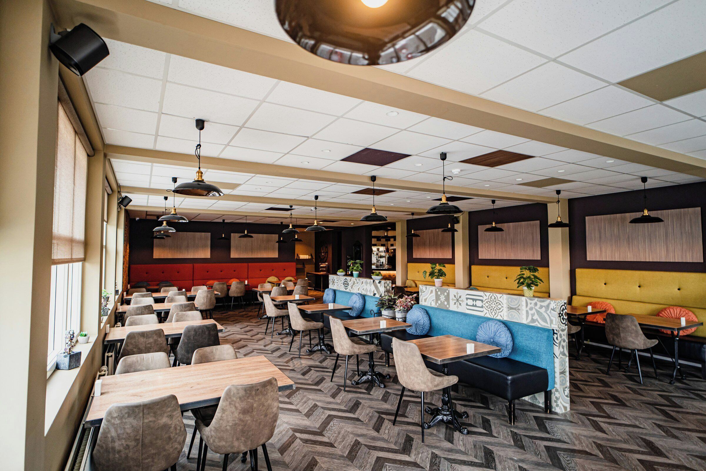A restaurant with a herringbone floor pattern, booths, and tables.