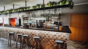 Zona de bar con pared de piedra, taburetes y una variedad de botellas y vasos.