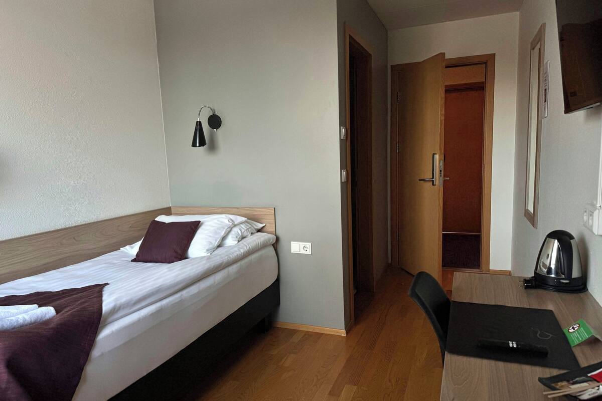 Ein Hotelzimmer mit Bett, Schreibtisch, Stuhl, einer Kaffeemaschine und einer Tür zu einem weiteren Raum.