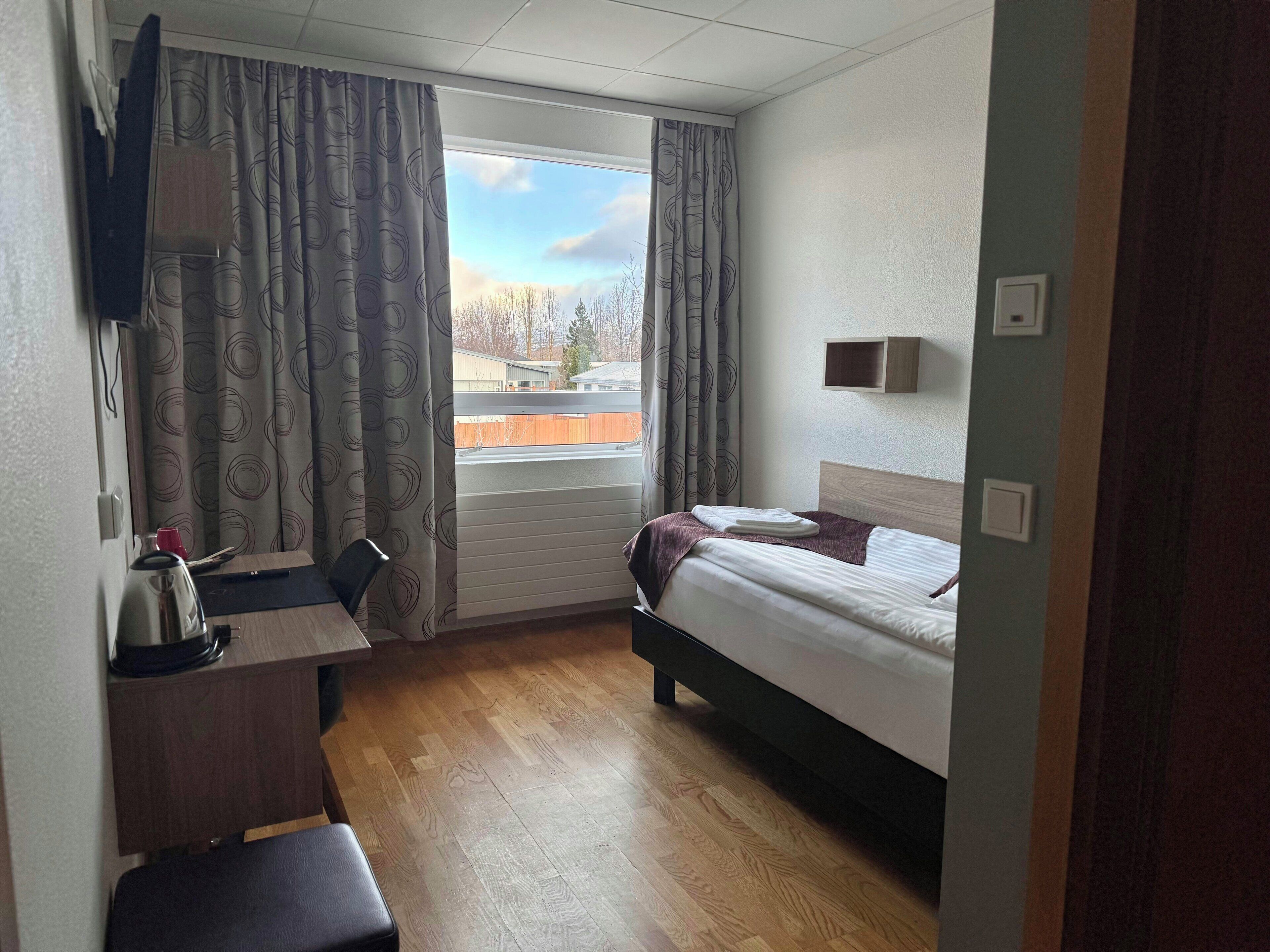 Habitación de hotel con cama, escritorio, silla y ventana con cortinas.