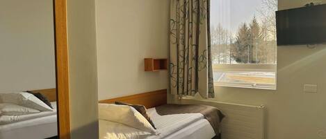 Un dormitorio con una cama, una ventana con cortinas, un televisor montado y un radiador.