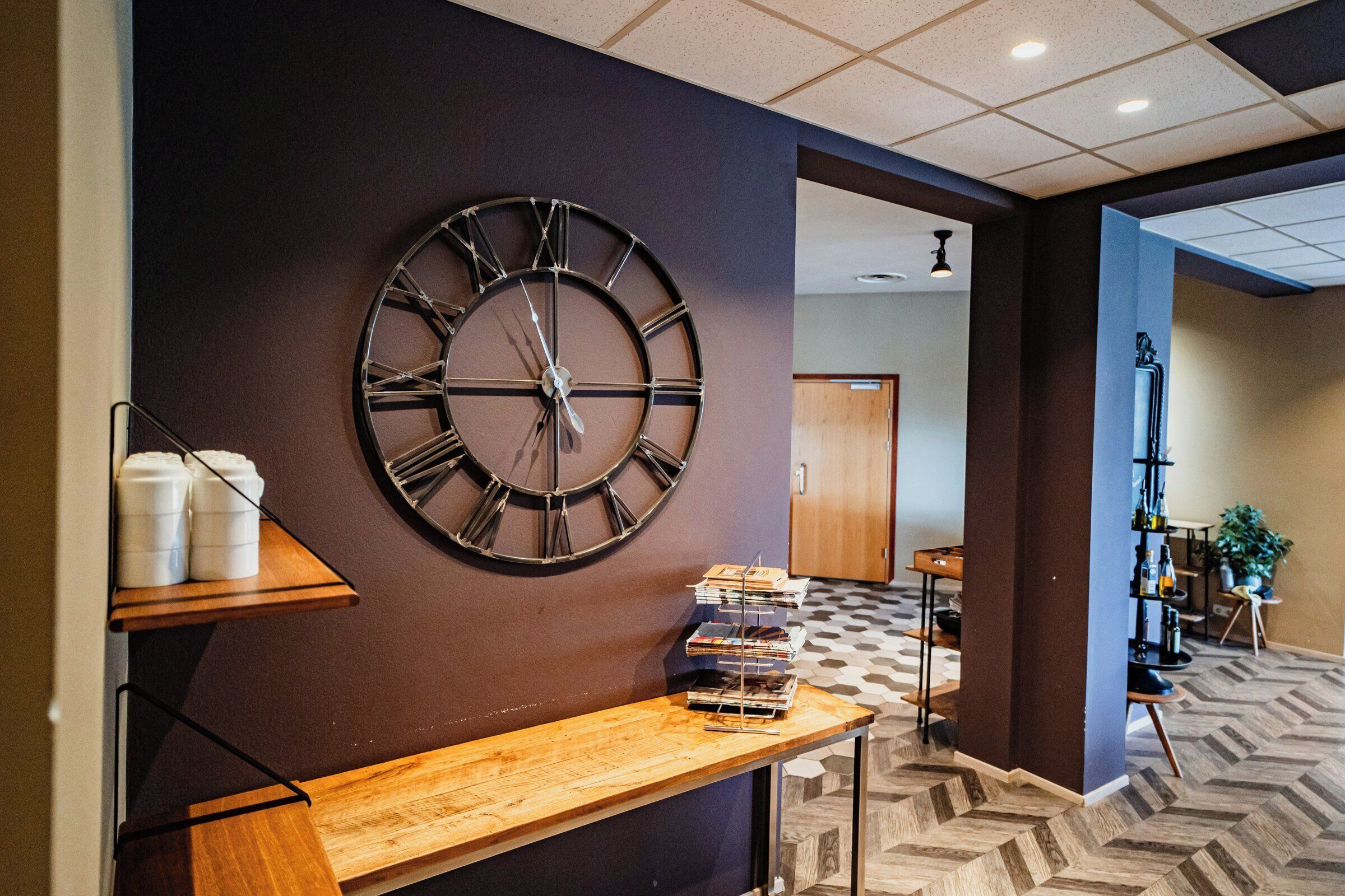 A hallway with a large wall clock, a wooden bench, and a bookshelf.