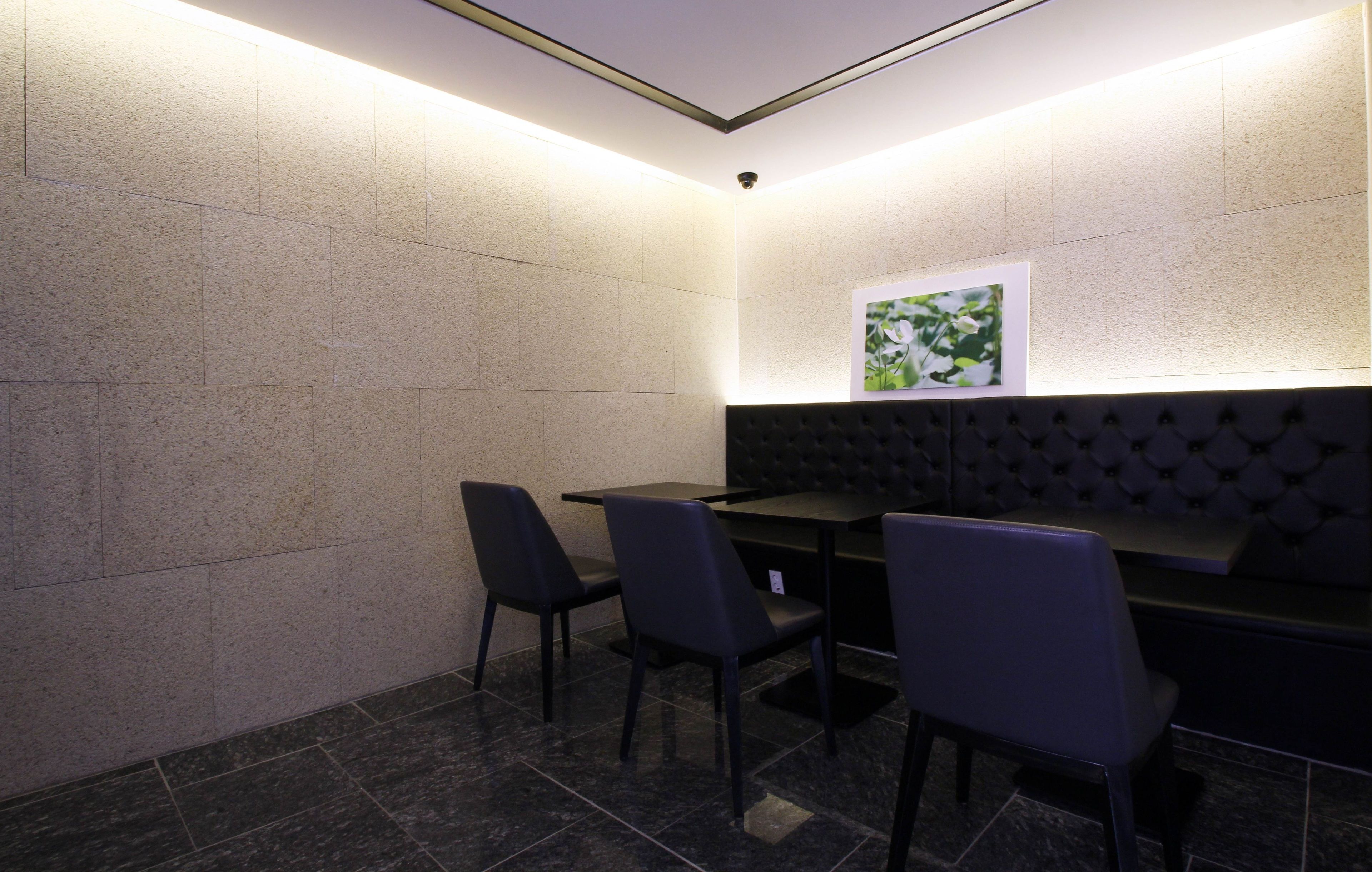 A corner seating area with a black cushioned bench and two chairs, a framed picture on the wall, and a ceiling light.