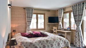 A bedroom with a bed, a desk, a chair, a television, and curtains. - Hôtel Les Mélèzes (Evolène)