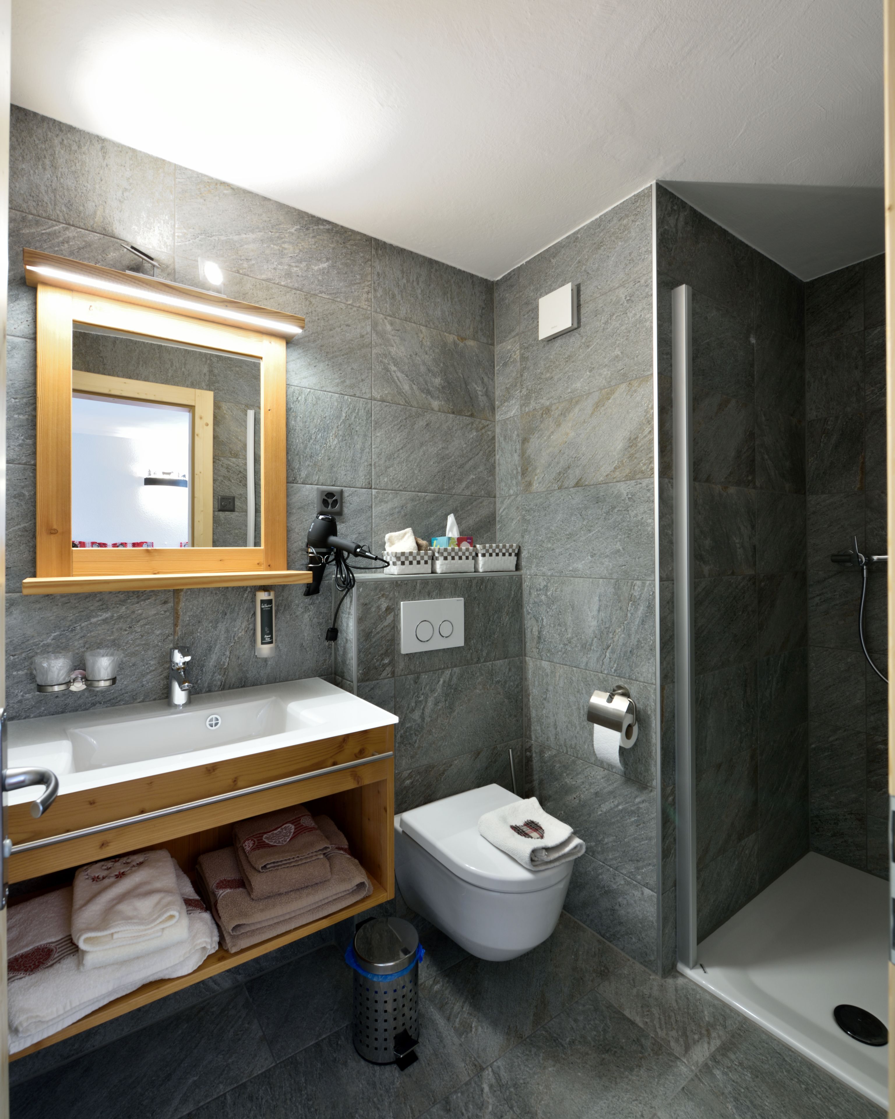Un baño moderno con un espejo grande, lavamanos blanco y zona de ducha.