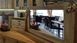 A rustic kitchen with wooden cabinets, a stone accent wall, and a view of the dining area. - Hôtel Les Mélèzes (Evolène)
