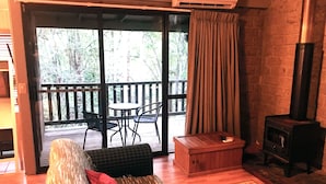 Um quarto aconchegante com um banco de madeira, uma mesa pequena, um sofá com almofada vermelha, um baú de madeira e uma lareira.