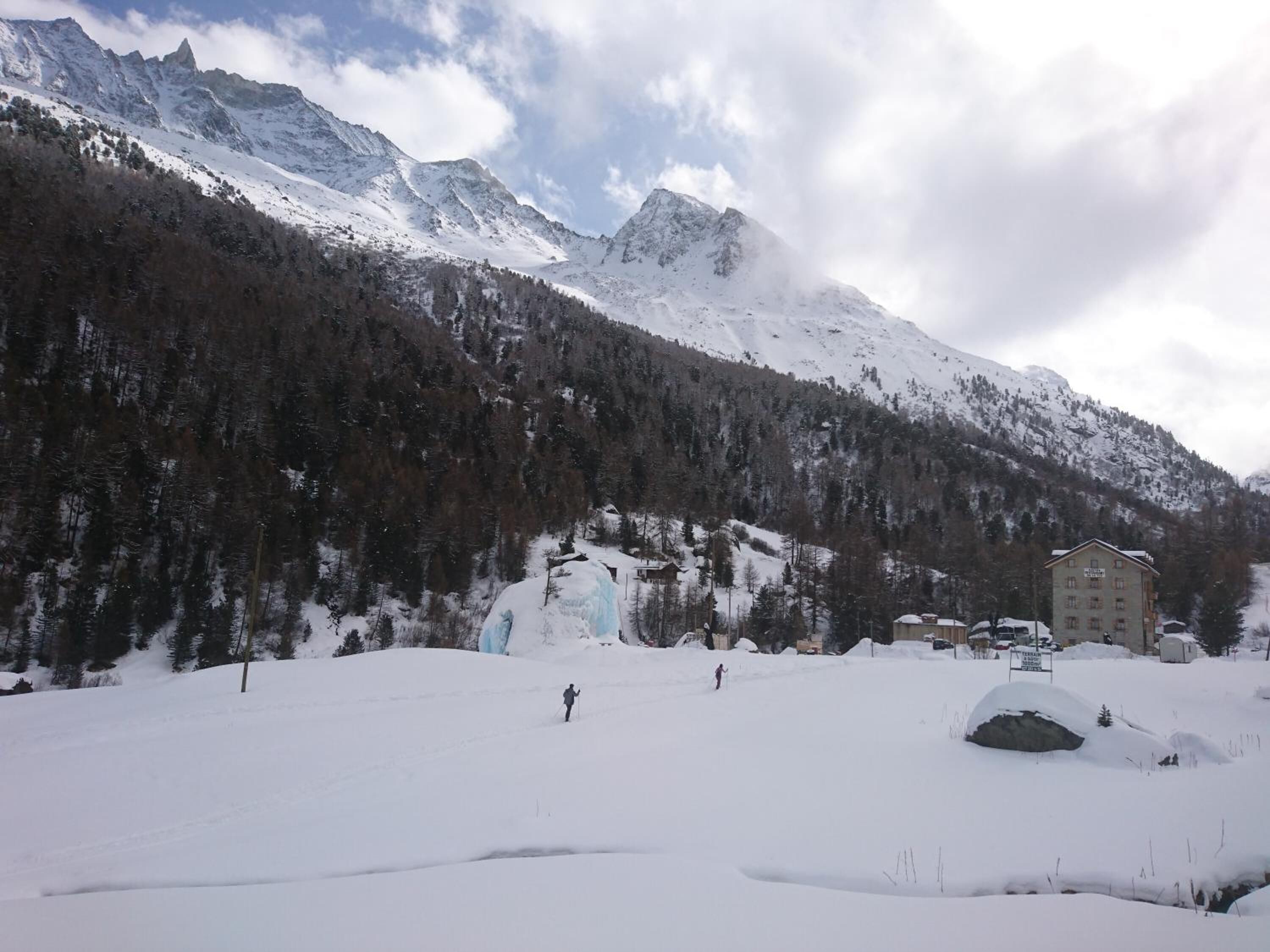 Un paysage enneigé avec une montagne, un bâtiment doté de nombreuses fenêtres et une personne qui fait du ski.