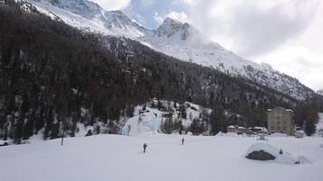 Un paysage enneigé avec une montagne, un bâtiment doté de nombreuses fenêtres et une personne qui fait du ski.