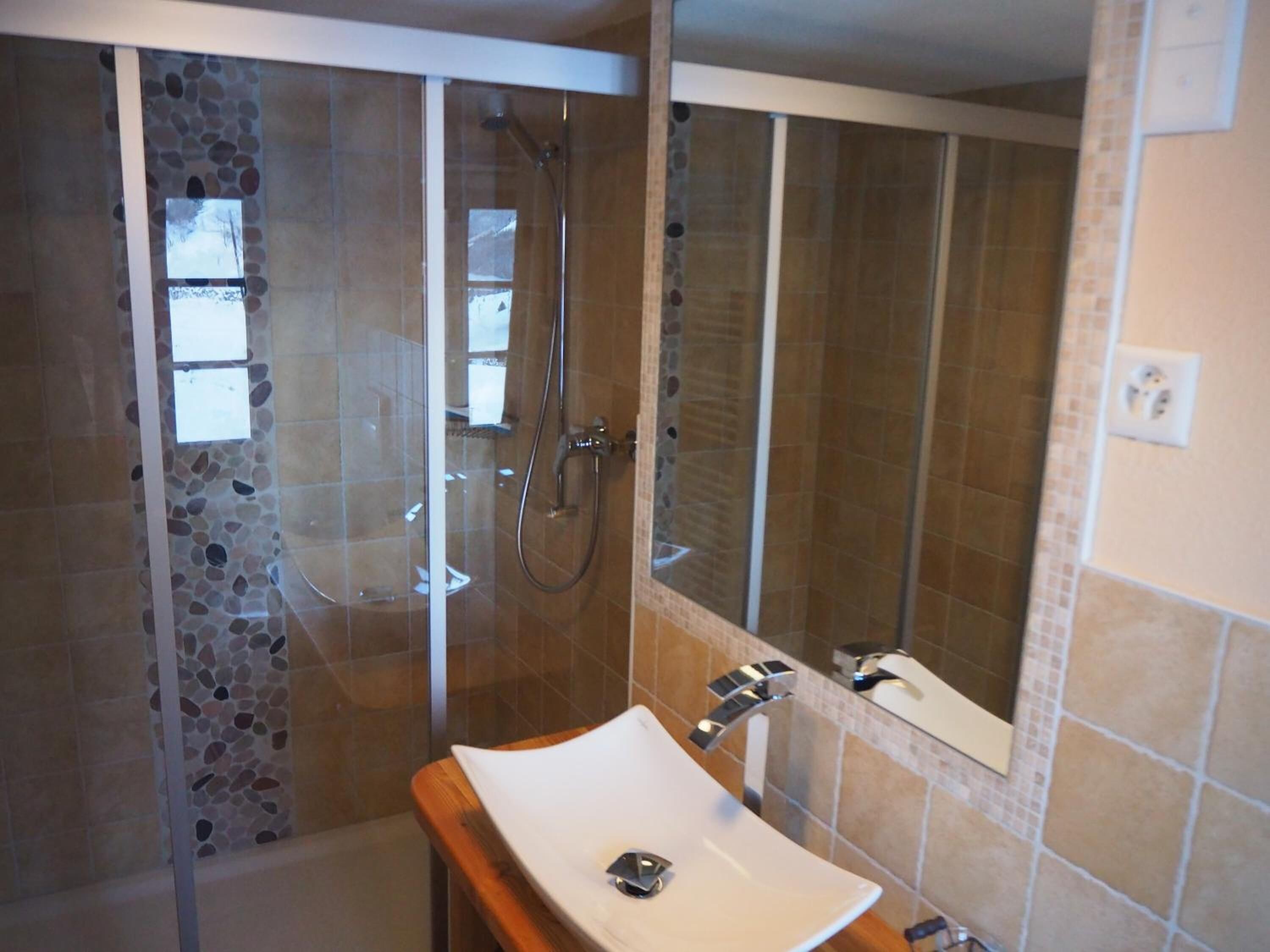 A bathroom with a glass-enclosed shower, a white sink, and a mirror.