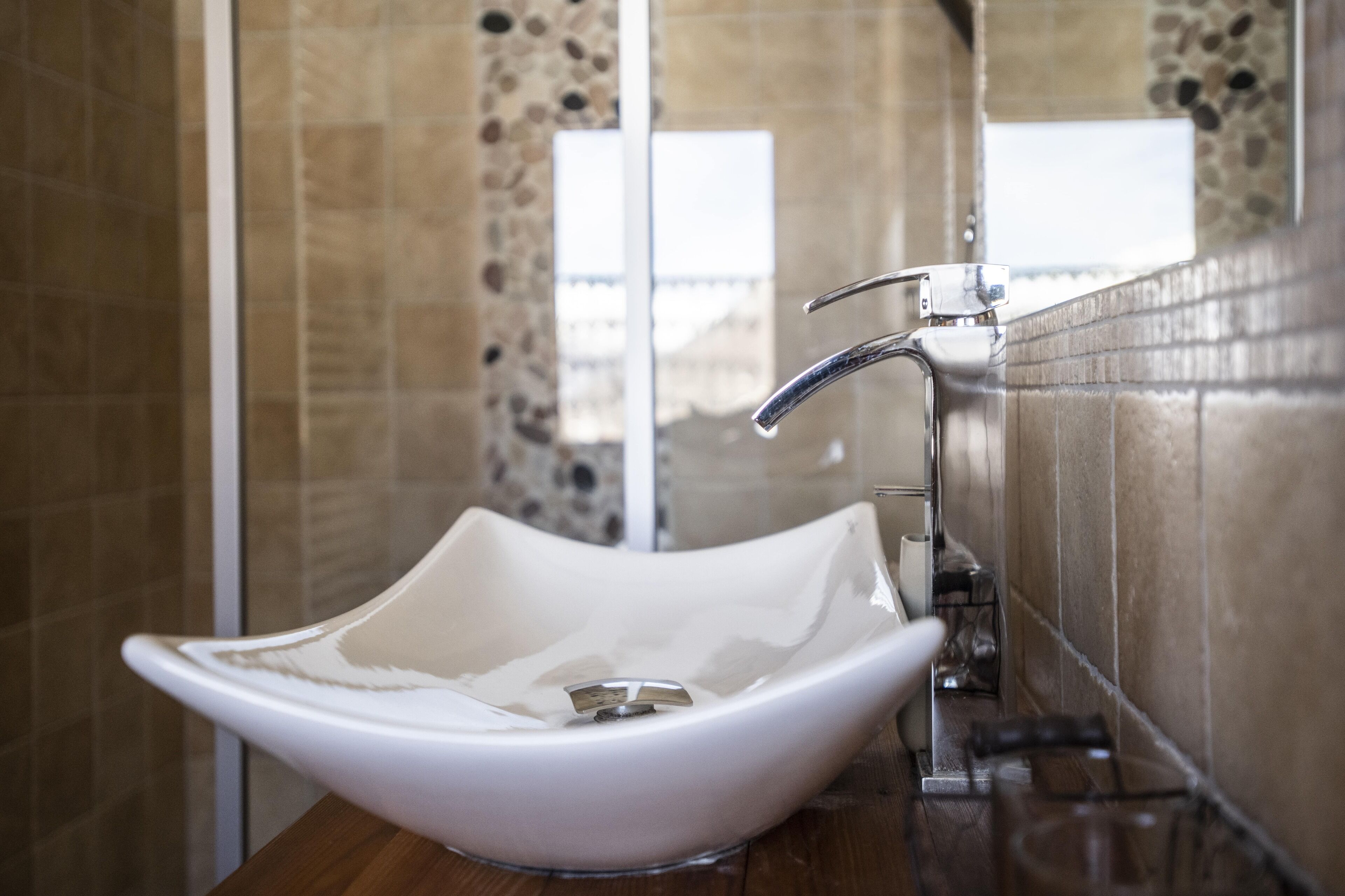 A modern bathroom with a white vessel sink, chrome faucet, and stone-patterned tiles.