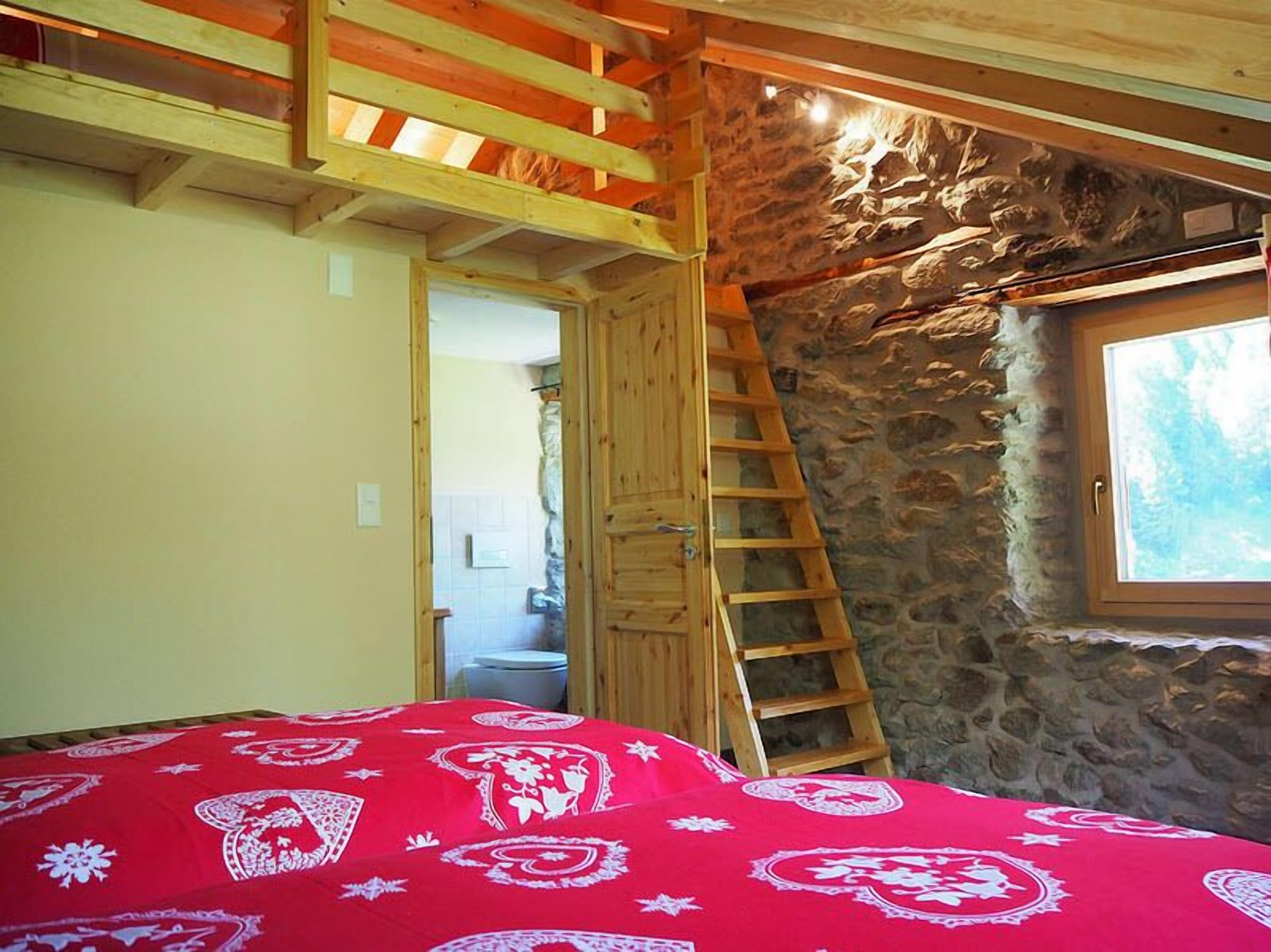 A bedroom with a wooden ladder, a stone wall, and a window.