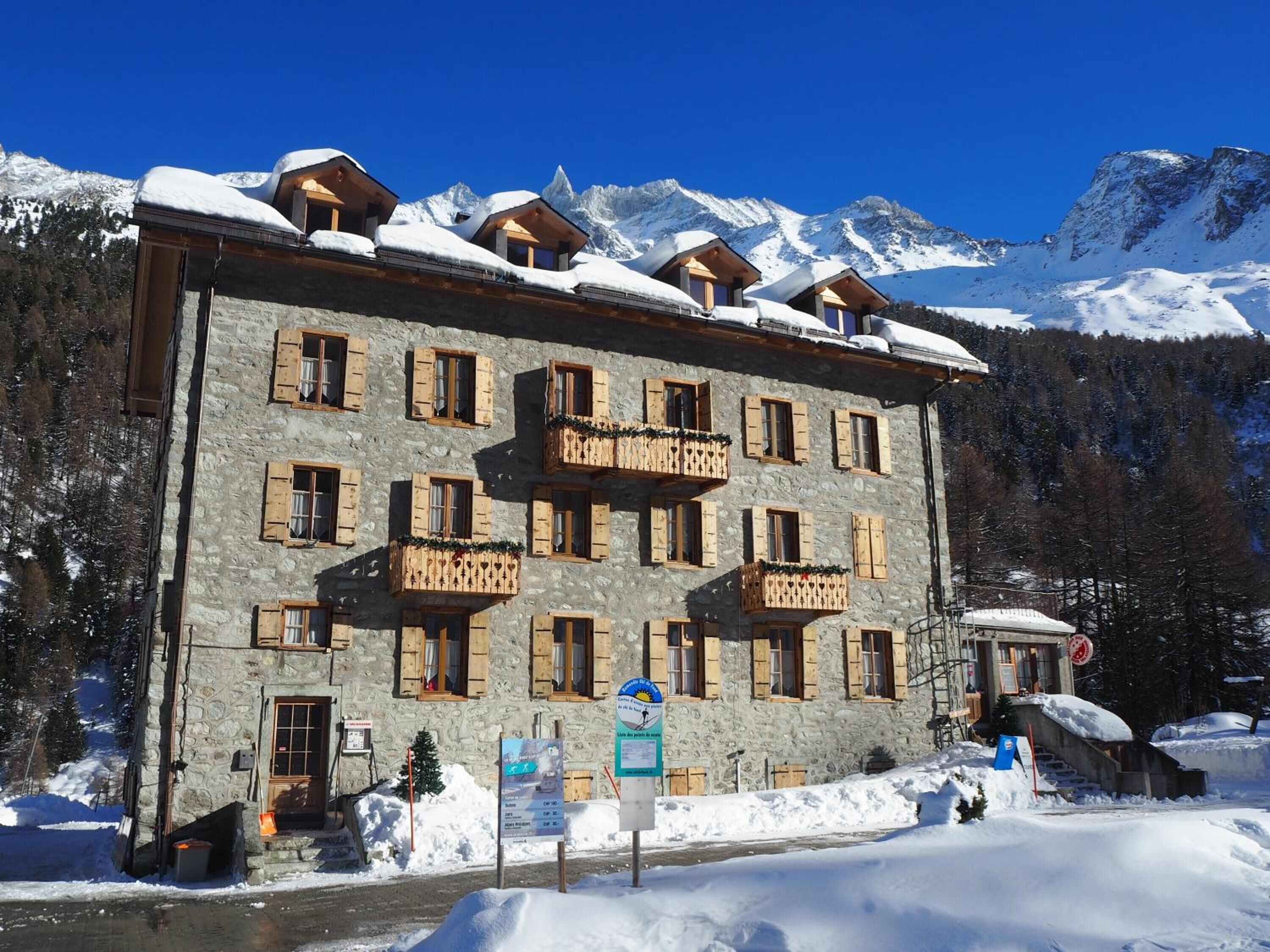 A stone building with multiple balconies, surrounded by snow-covered mountains.