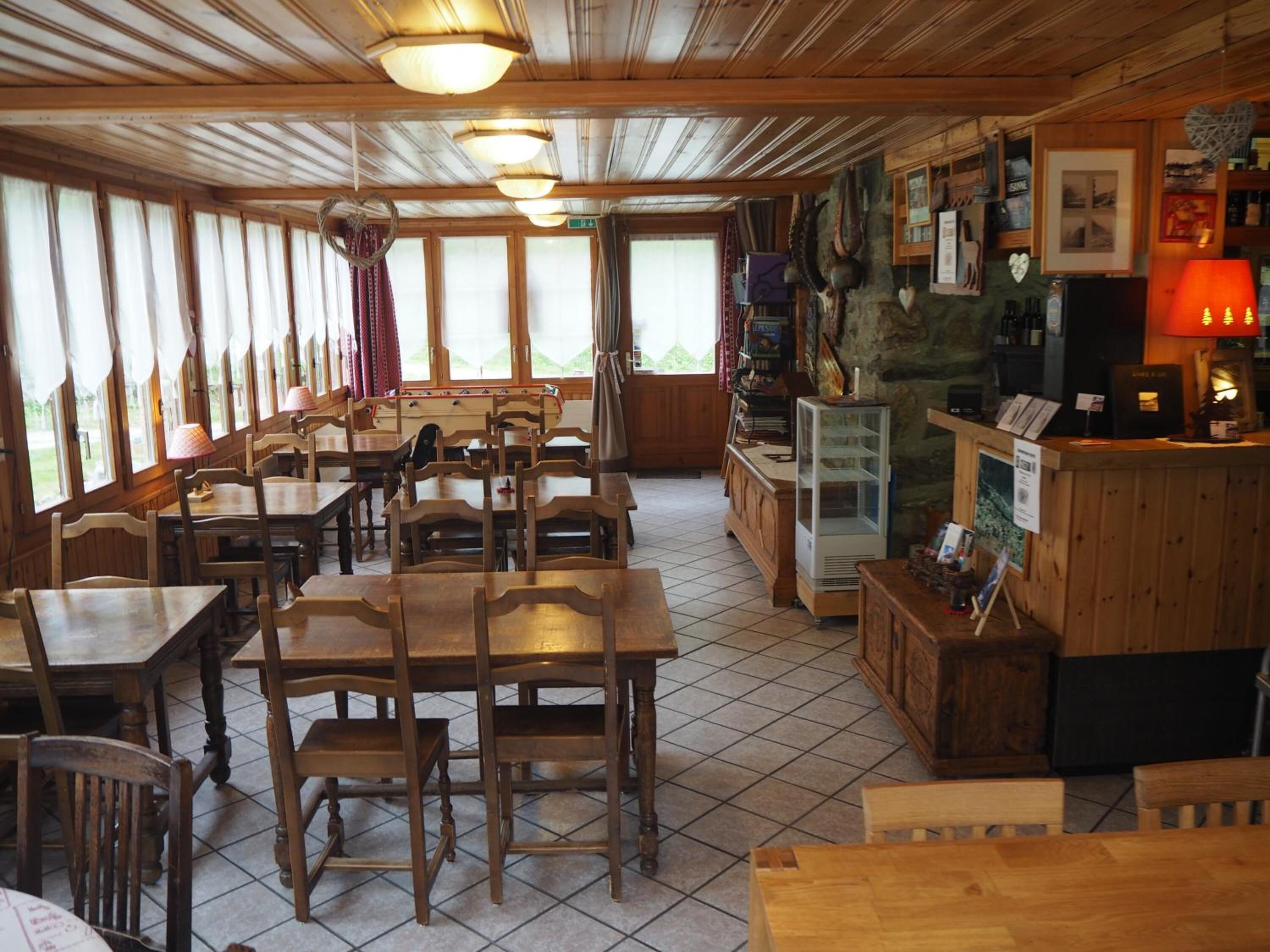 A cozy restaurant with wooden tables and chairs, a bar area with a red lamp, and a view of the outdoors through large windows.