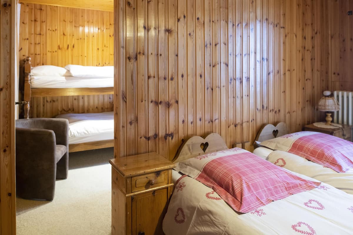 Una habitación de cabaña de madera con literas, una mesita de noche de madera, una silla y una lámpara.