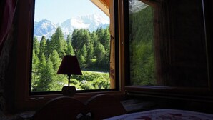 Una habitación con cama, ventana y vistas a un bosque y montañas.