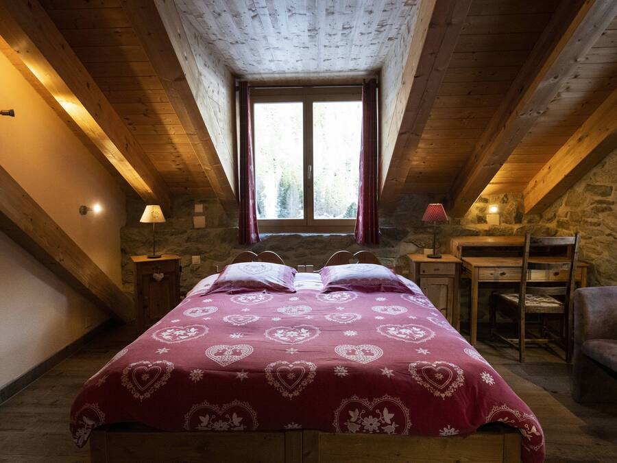 Un dormitorio con techo de madera, una cama grande con ropa de cama estampada con motivos de corazón, un escritorio y una silla.