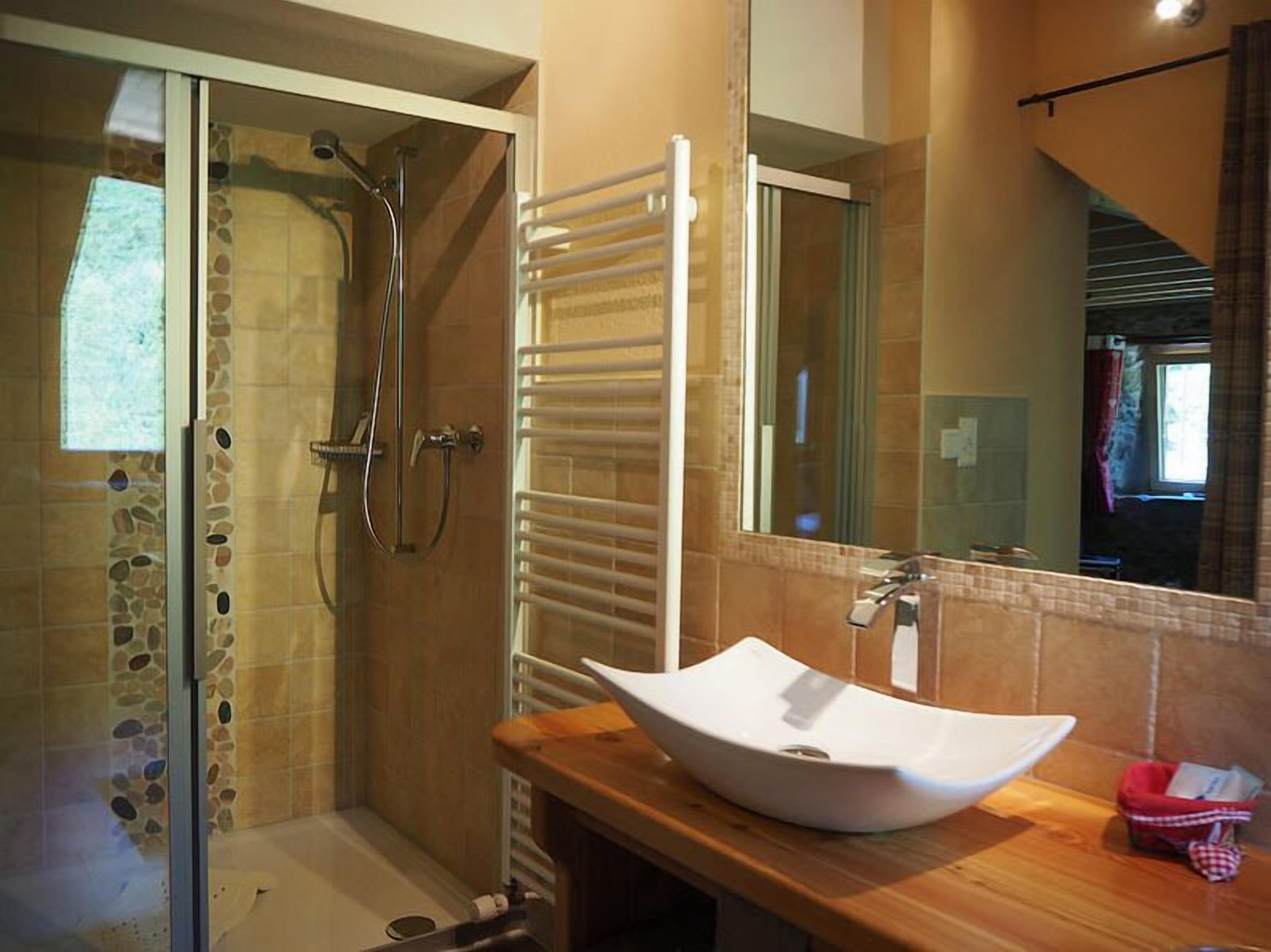 A modern bathroom with a glass-enclosed shower, a white vessel sink, and a large mirror.