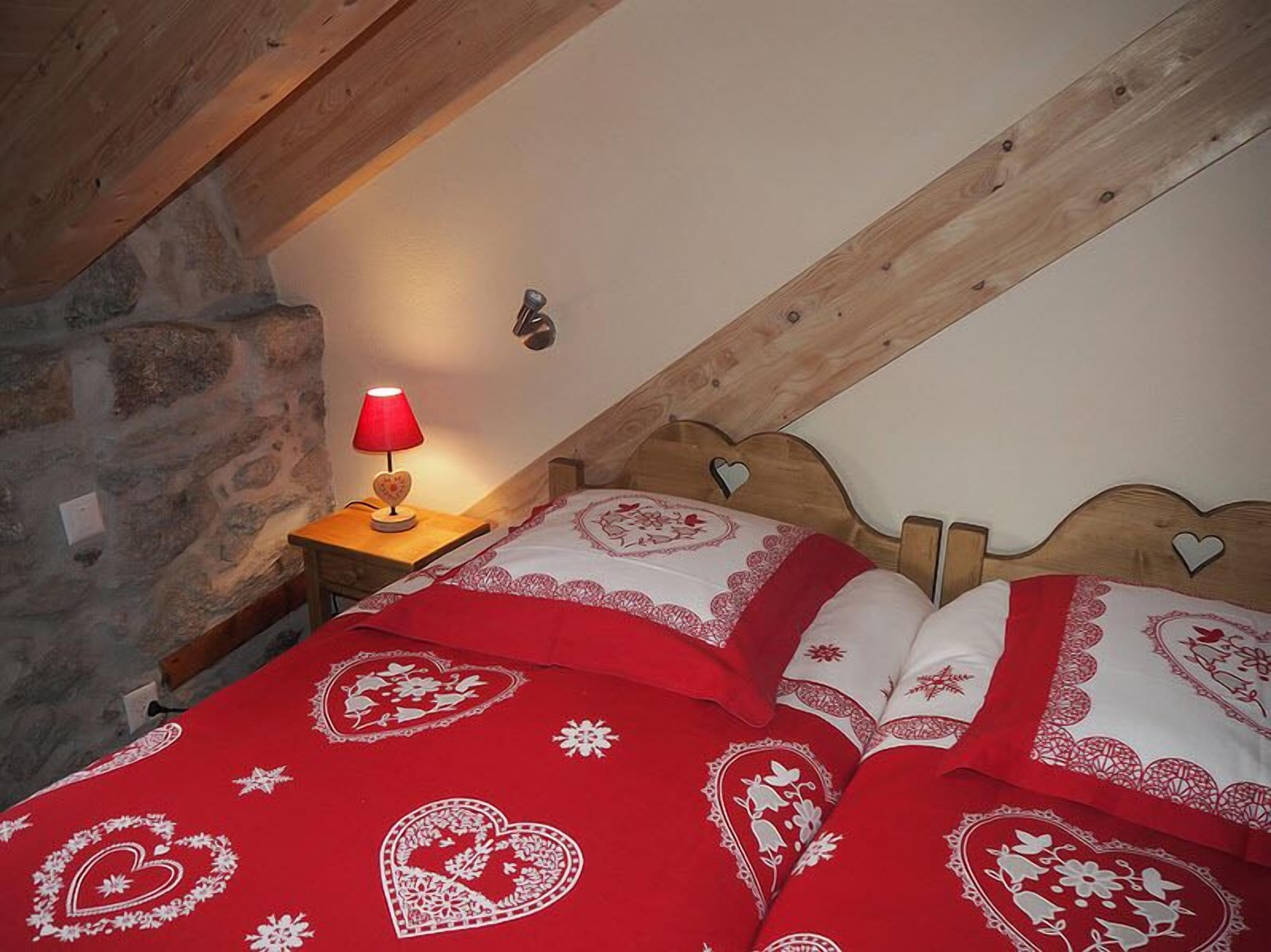 Un dormitorio acogedor con techo inclinado, pared de piedra, cabecera de madera y mesita de noche con lámpara.