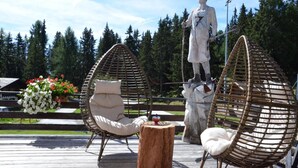 A statue of a man holding a staff, surrounded by wicker chairs and a wooden table on a wooden deck. - Hôtel Restaurant LA CAMBUSE (Vex)