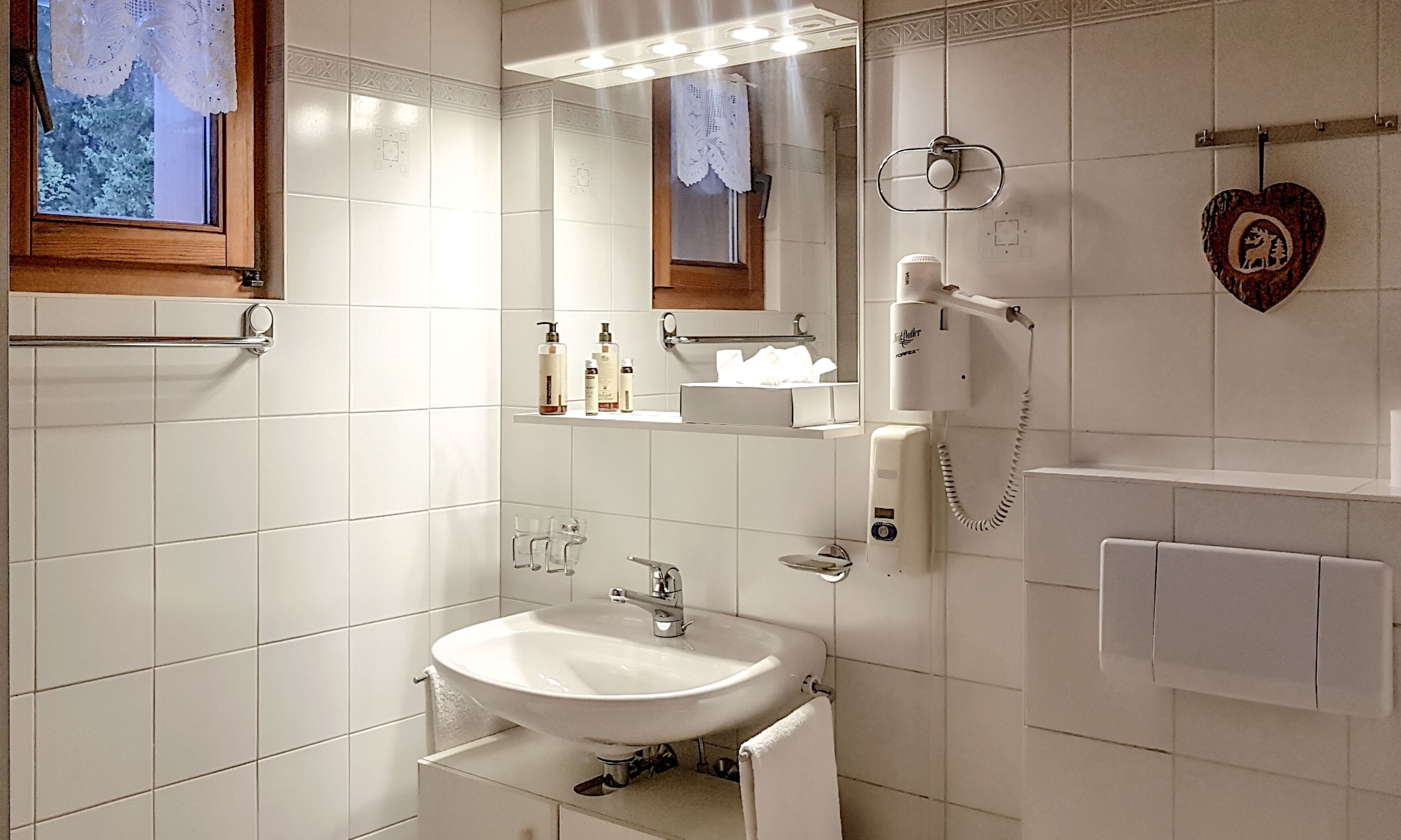 A modern bathroom with a white sink, a mirror, and a hairdryer on the wall.