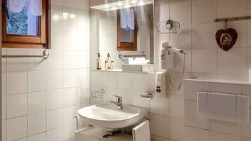 A modern bathroom with a white sink, a mirror, and a hairdryer on the wall.