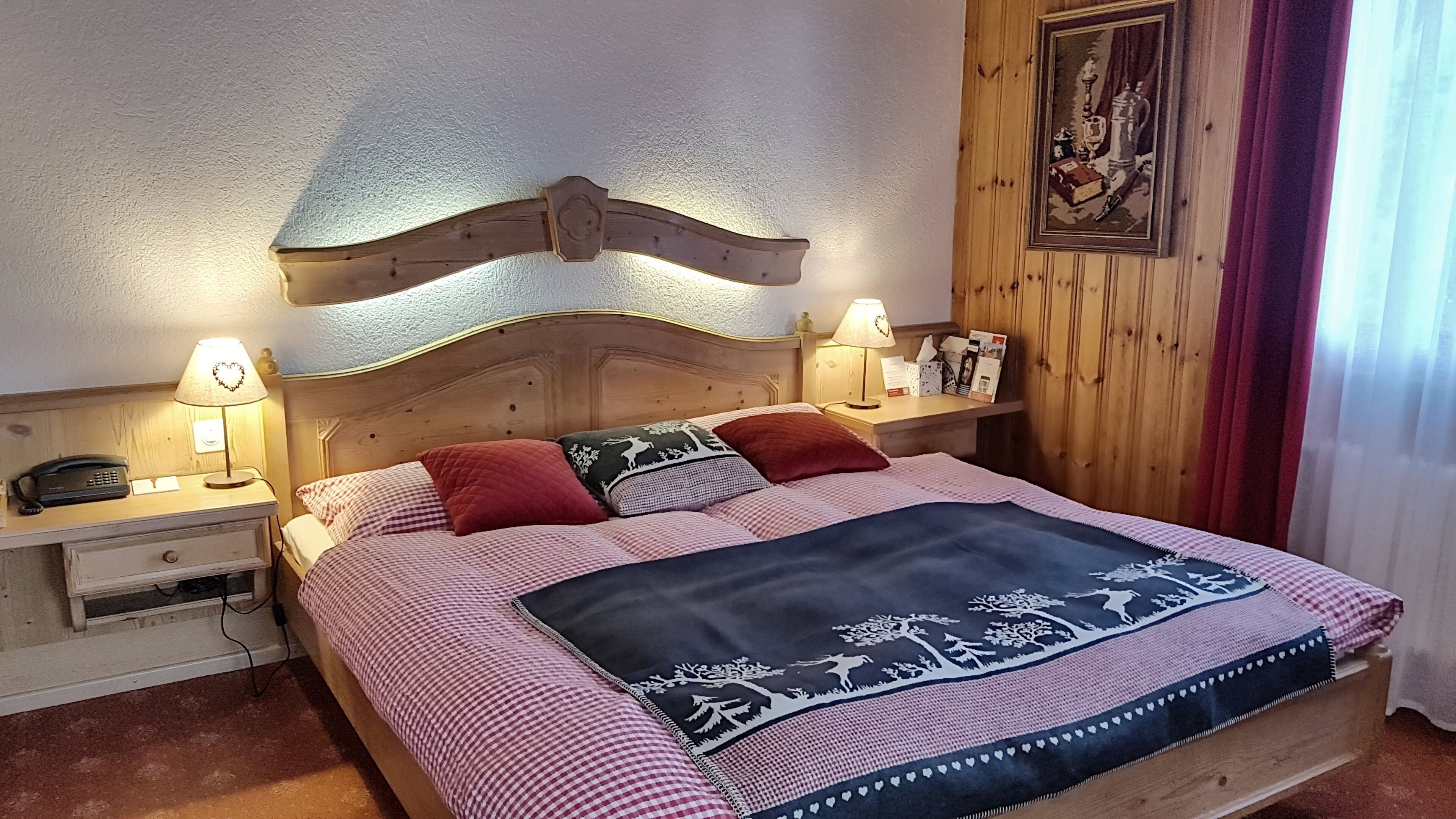 A bed with a wooden headboard, two bedside tables with lamps, a checkered bedspread, and a wall-mounted picture.
