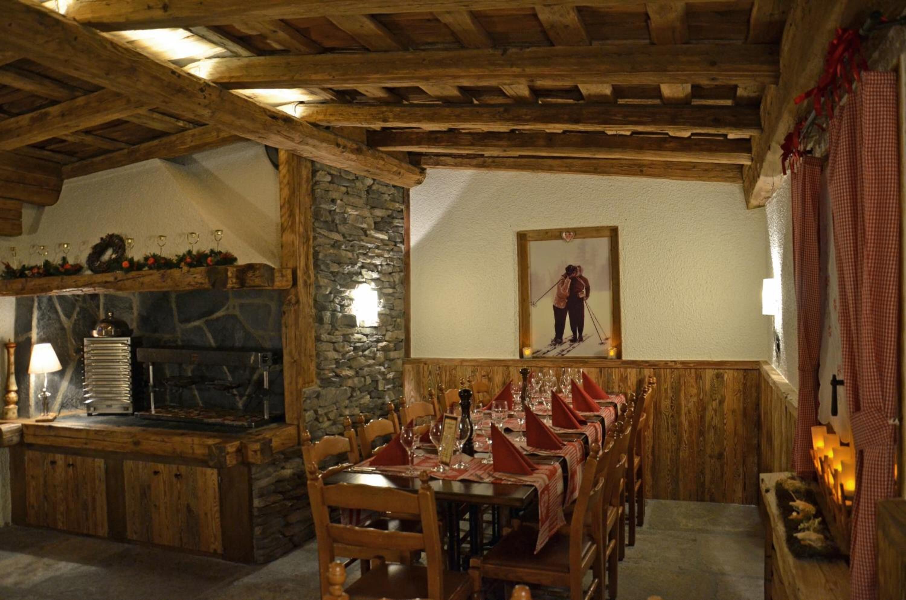 A rustic dining area with wooden tables and chairs, a stone fireplace, and a ski-themed painting on the wall.