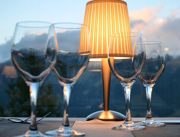 Three wine glasses and a lamp on a table with a mountain view in the background. - Hôtel Restaurant LA CAMBUSE (Vex)