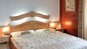 Una cama bien hecha con cabecera de madera, dos mesitas de noche con lámparas y un cuadro enmarcado en la pared.