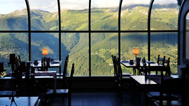 A dining area with tables and chairs, large windows offering a view of green mountains and valleys. - Hôtel Restaurant LA CAMBUSE (Vex)