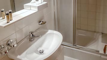 Un baño con un lavamanos blanco, grifo de cromo y un espejo encima. Hay tres botellas en el borde del lavamanos y una caja de pañuelos sobre el espejo.