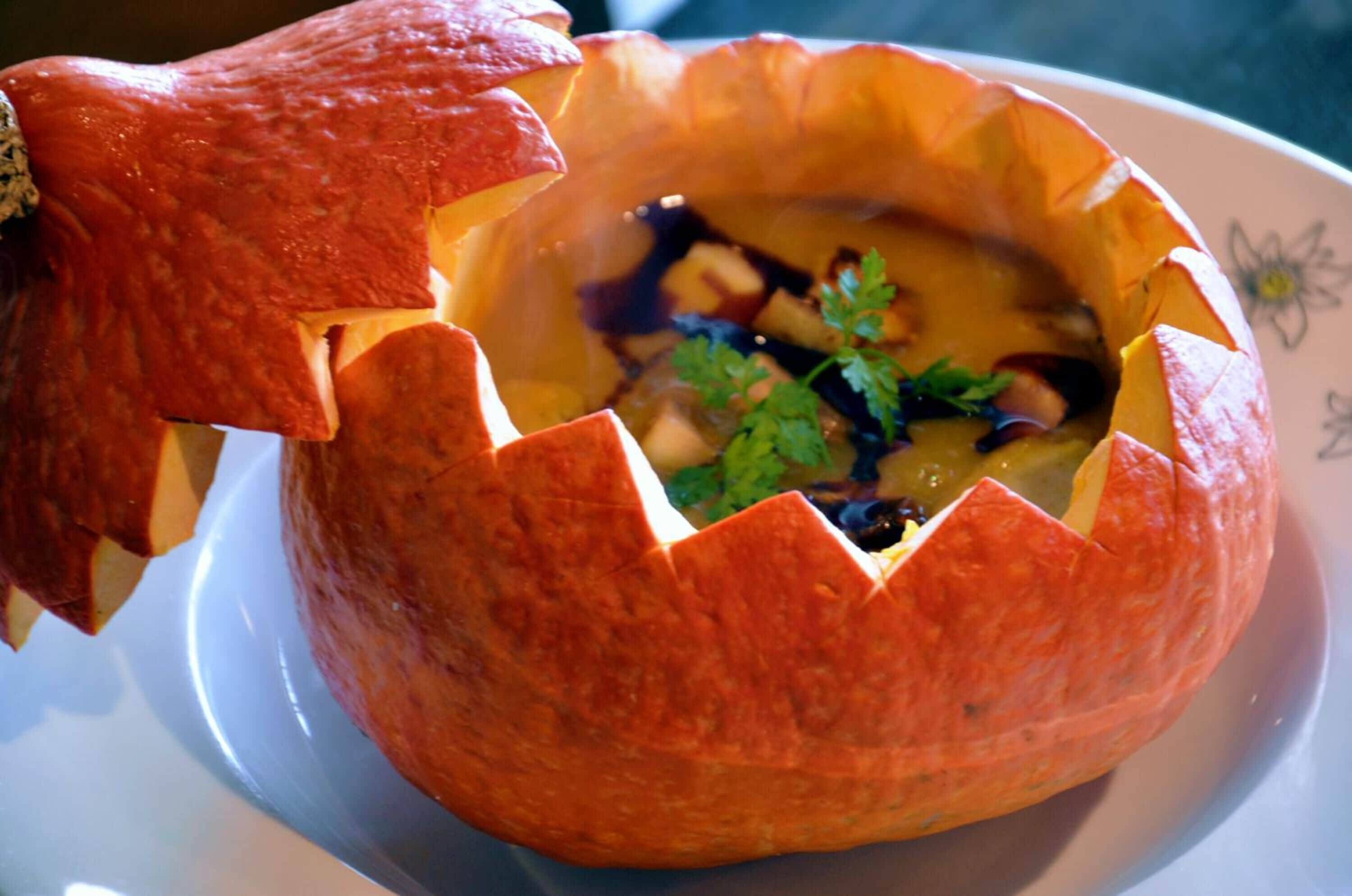 Un tazón de calabaza tallado, lleno de sopa y adornado con perejil.