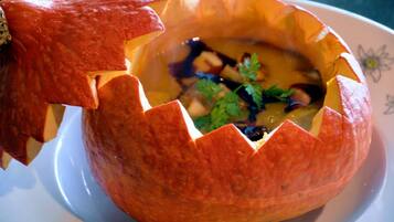 Un tazón de calabaza tallado, lleno de sopa y adornado con perejil.