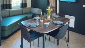 Una sala de estar moderna con comedor, un sofá, un televisor montado en la pared y una ventana con cortinas.