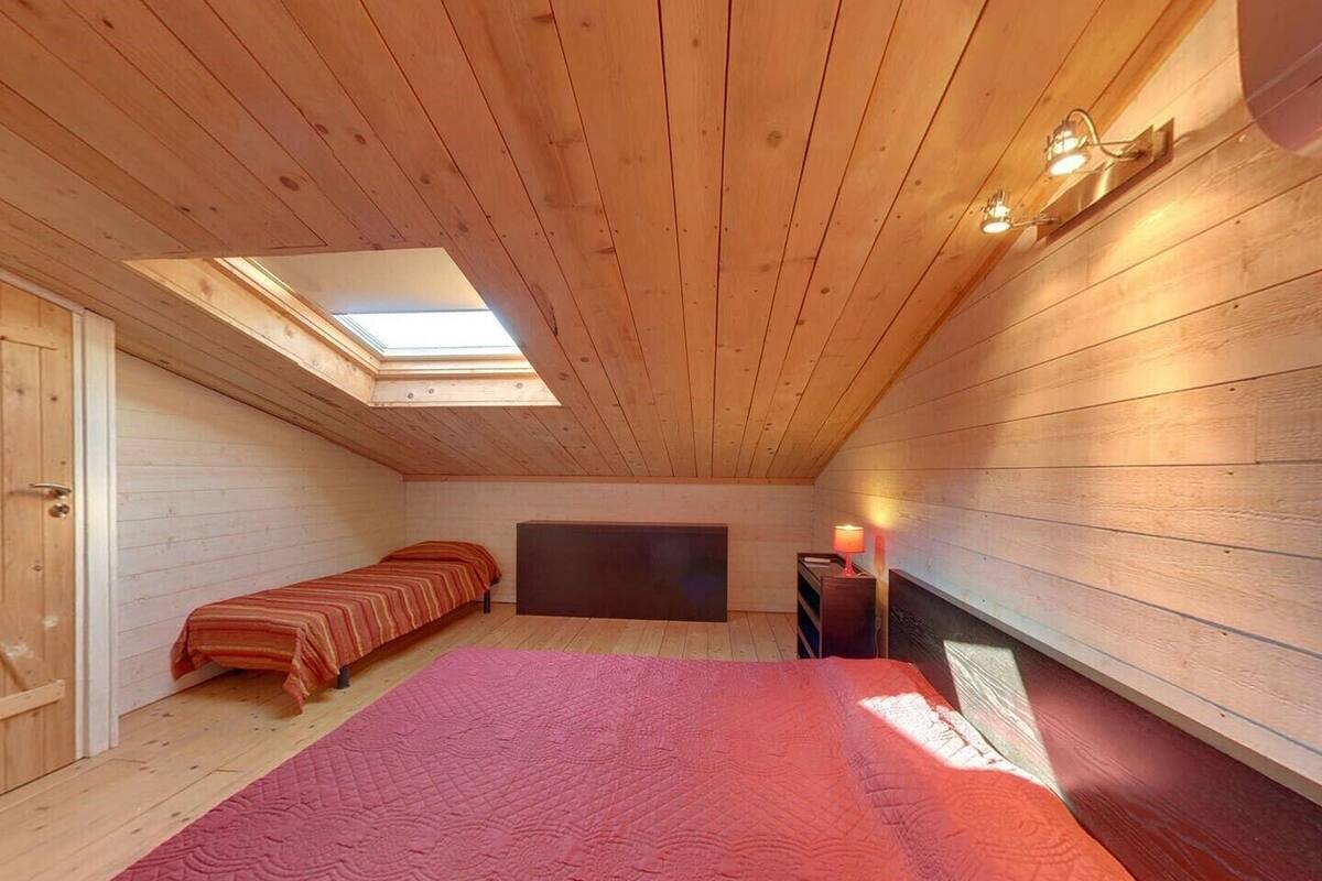 Un dormitorio acogedor en el ático con tragaluces, una cama, una mesita de noche con lámpara y una chimenea.