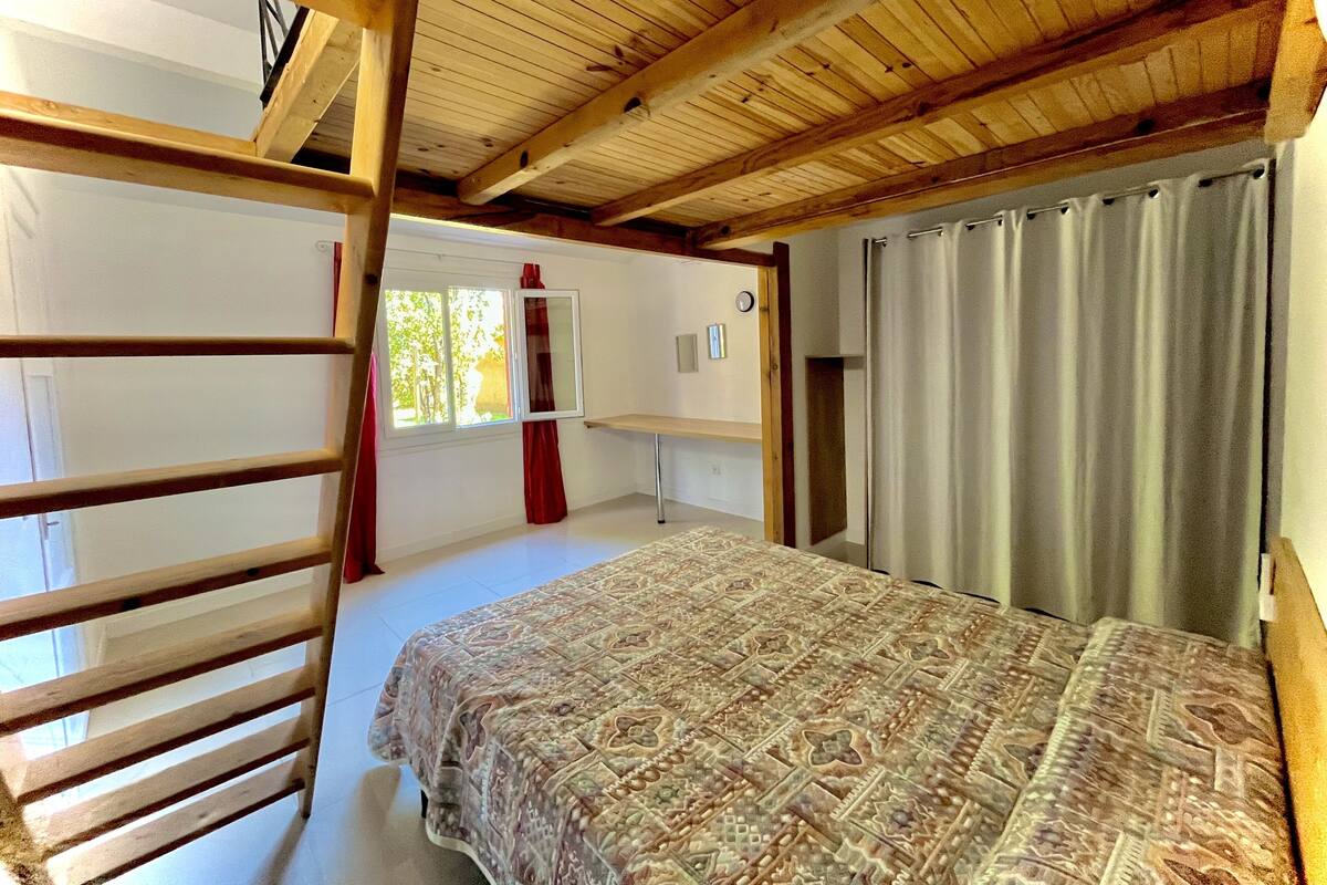 Un dormitorio con cama, vigas de madera en el techo, una ventana con cortinas y una puerta.