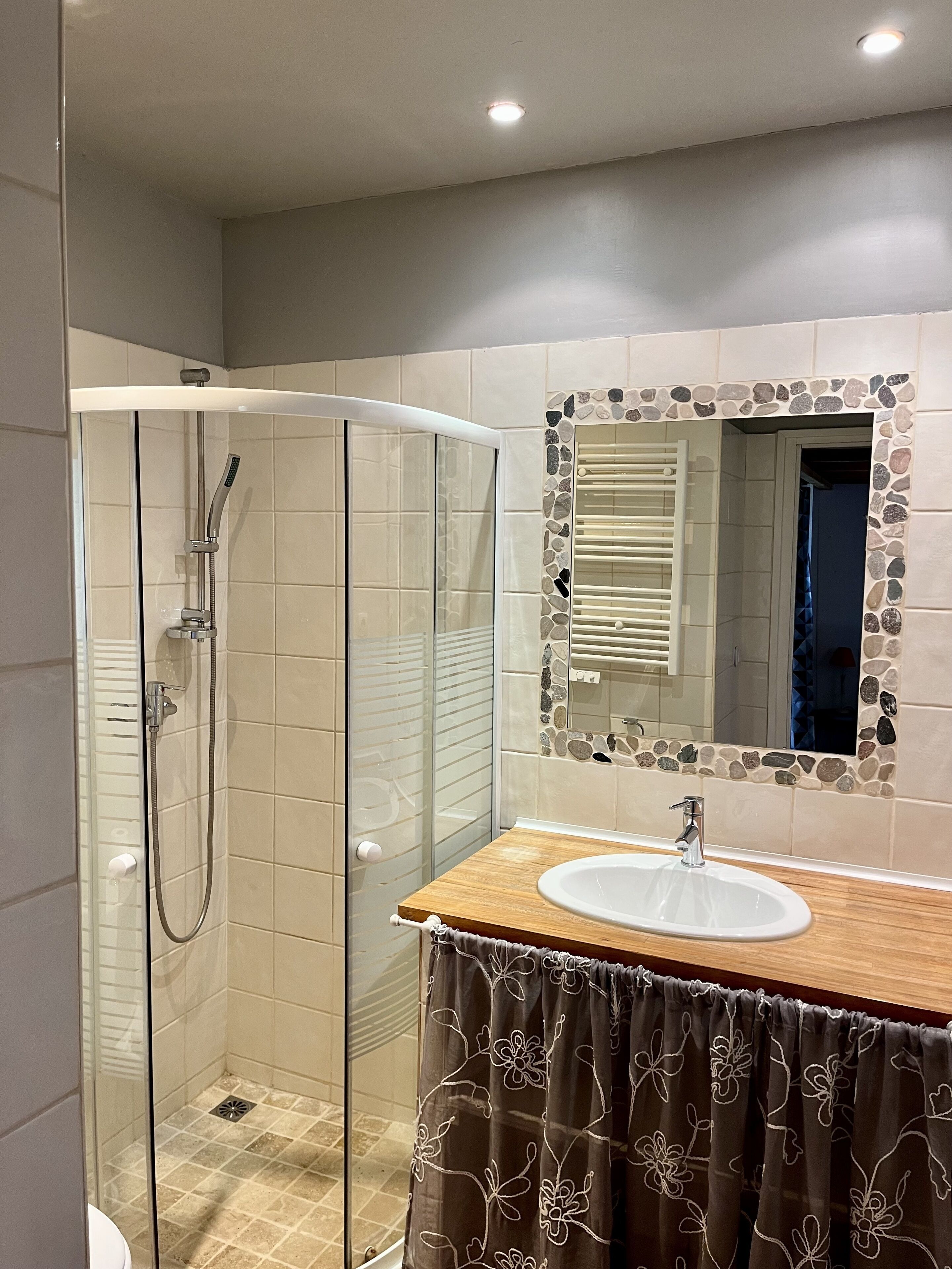 Une salle de bain moderne dotée d’une douche à parois de verre, d’un meuble-lavabo en bois et d’un miroir orné d’un cadre en pierre.
