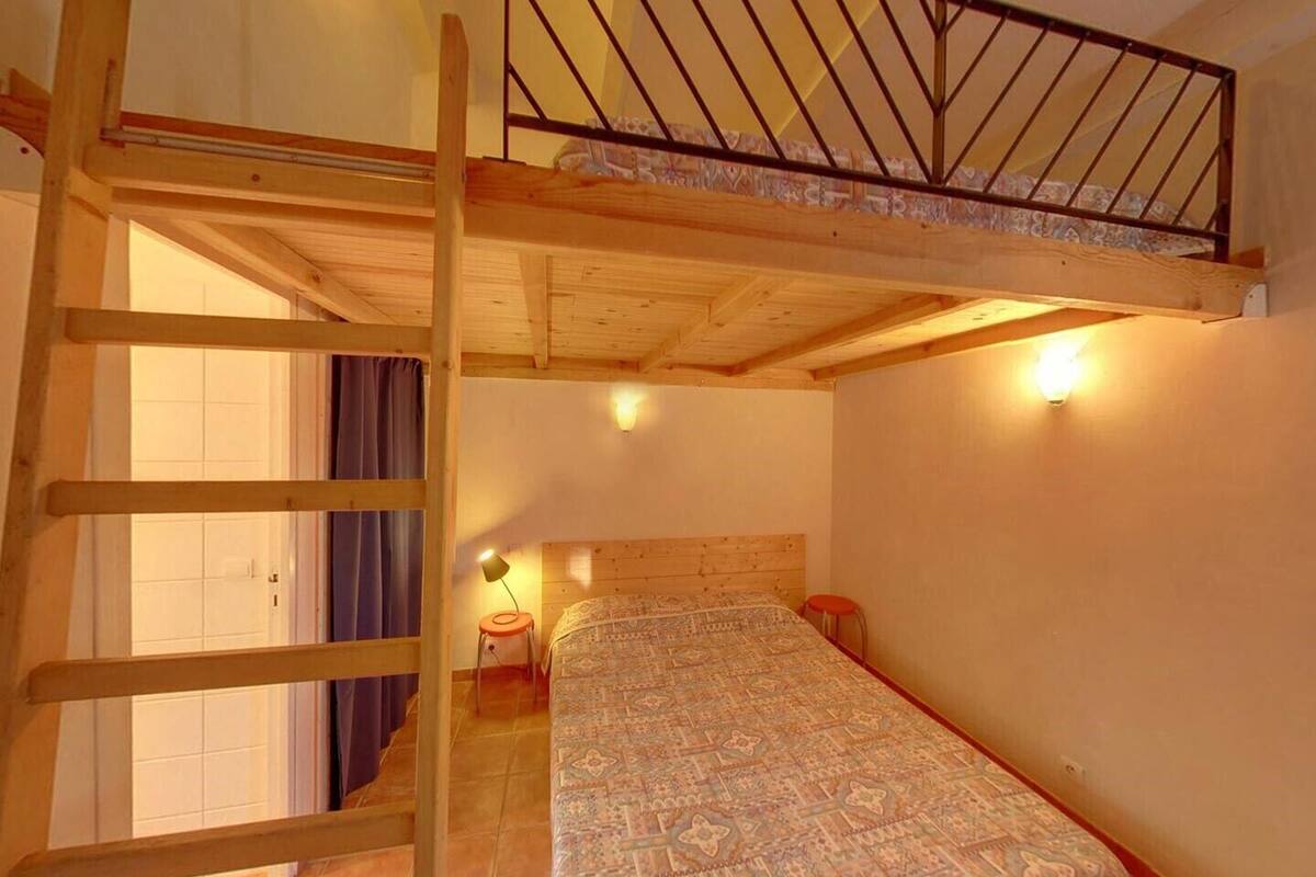 Una habitación con una cama litera, una escalera, una mesita y un aplique de pared.
