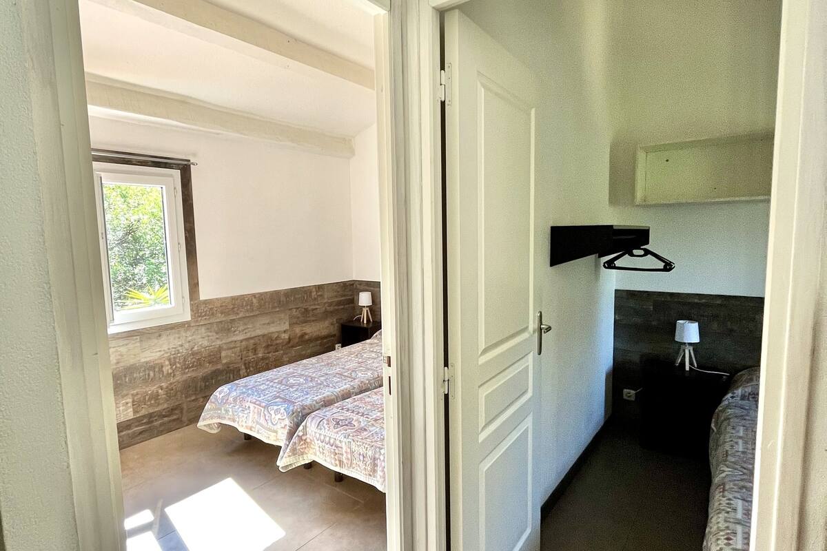 Una habitación con dos camas, una ventana, una puerta y una pequeña mesa con lámpara.