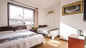 A hotel room with two beds, a window with curtains, an air conditioning unit, a painting on the wall, and a wooden cabinet.