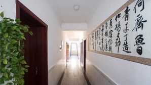 A hallway with a large calligraphy wall, a wooden door, and a potted plant.