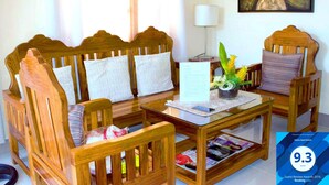 A wooden sofa set with cushions, a glass coffee table with a menu and a smartphone, and a framed artwork on the wall. - Haisa Apartment (Coron)