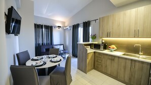 A modern kitchen with wooden cabinets, a microwave, and a sink. There is a dining area with a table and chairs. - Regalo Apartments (Lefkada)