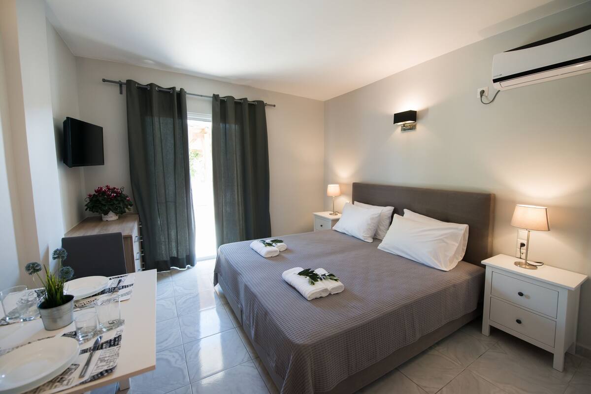 A hotel room with a bed, bedside tables, a TV mounted on the wall, and a window with curtains.
