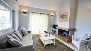 A modern living room with a sofa, coffee table, fireplace, and a view of the outdoors. - Regalo Apartments (Lefkada)