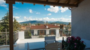 A terrace with a table and chairs, a bottle, and a basket of flowers. - Regalo Apartments (Lefkada)